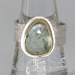 The picture shows a slightly oval aquamarine stone set in gold with a silver band 5 mm in diameter and with a textured surface